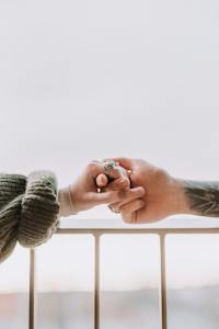 Crop unrecognizable tattooed man and woman in warm sweater holding hands on balcony on cloudy day