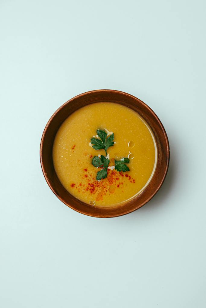 Top view of fresh pumpkin cream soup decorated with herbs and paprika served in bowl on white background in room